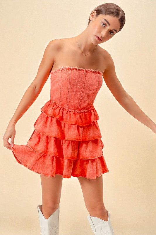 Woman wearing a coral strapless dress with ruffled layers on a beige background