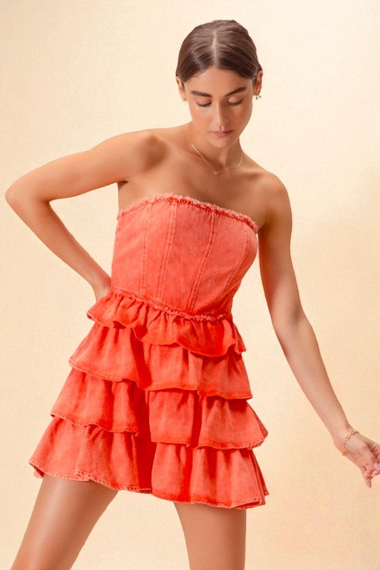 Woman wearing a coral strapless dress with ruffled layers on a beige background