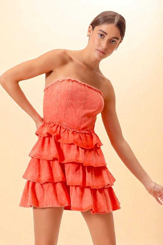 Woman wearing a coral strapless dress with ruffled layers on a beige background