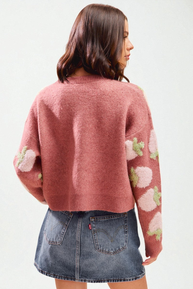 Person wearing a pink sweater with floral patterns and a denim skirt on a white background