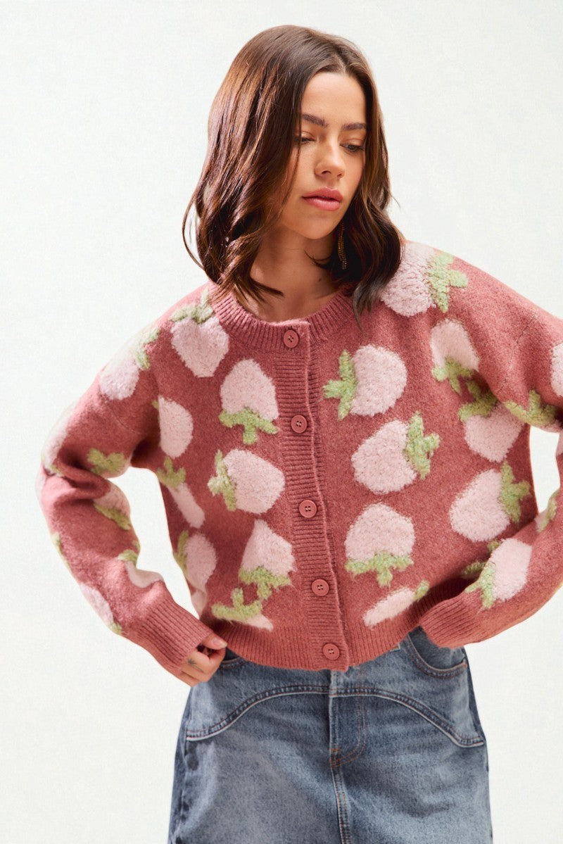 Woman wearing a pink sweater with white and green pattern on a white background