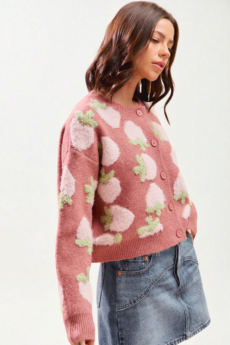 Woman wearing a pink sweater with floral patterns against a white background