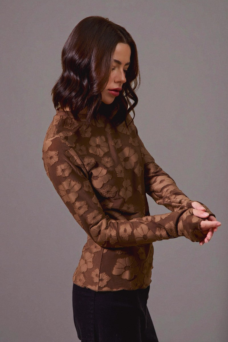 Woman wearing a brown patterned long-sleeve top against a gray background