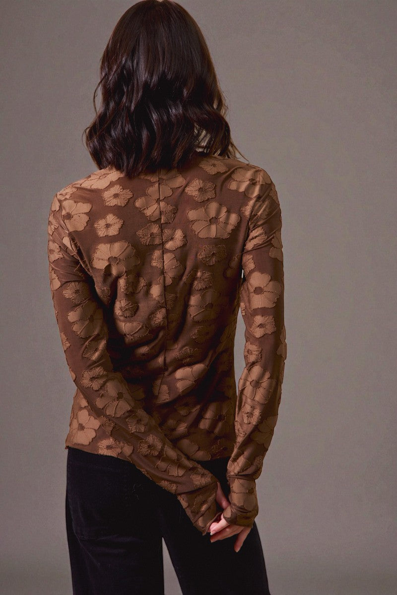 Person wearing a brown patterned long-sleeve shirt against a gray background