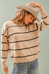 Woman wearing a beige sweater with black stripes and a straw hat against a light green background