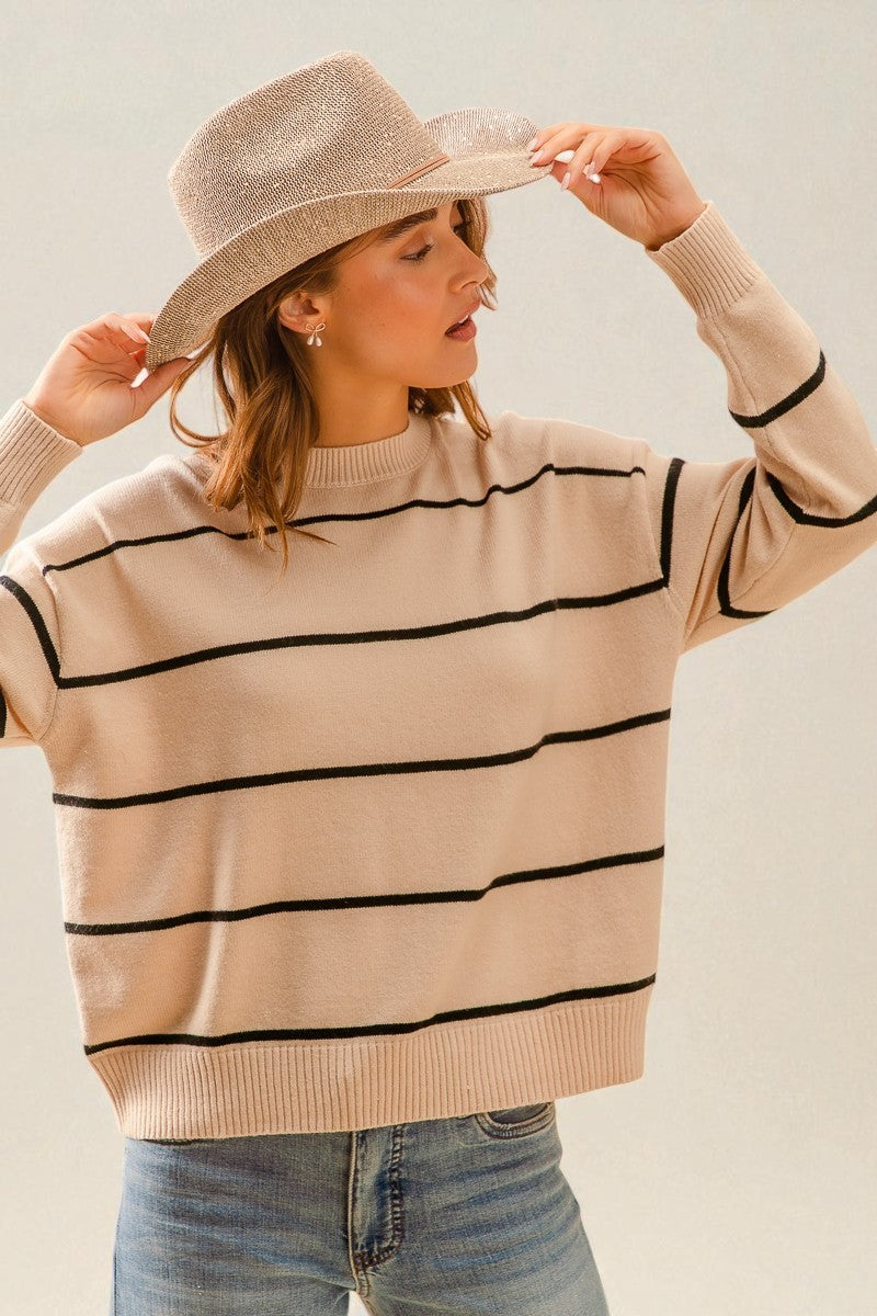 Woman wearing a beige sweater with black stripes and a matching hat against a plain background