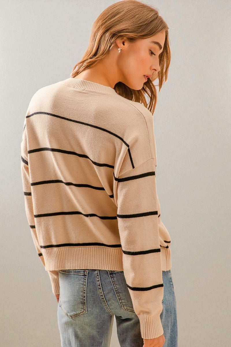 Woman wearing a beige sweater with black stripes and blue jeans against a plain background