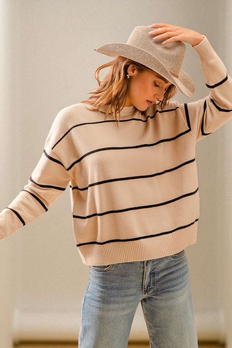 Woman wearing a beige sweater with black stripes and a beige hat indoors.