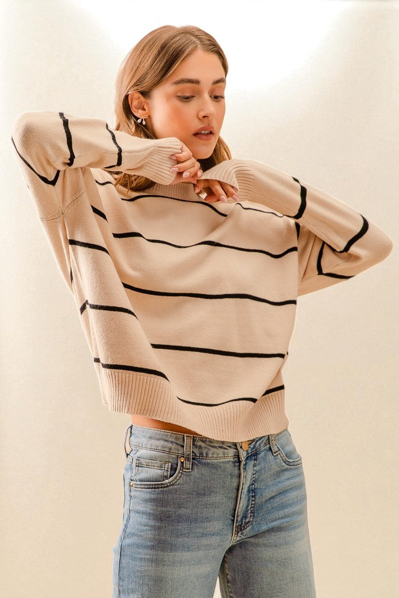 Woman wearing a beige sweater with black stripes and blue jeans on a plain background