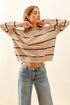 Woman wearing a beige sweater with black stripes and blue jeans on a light background