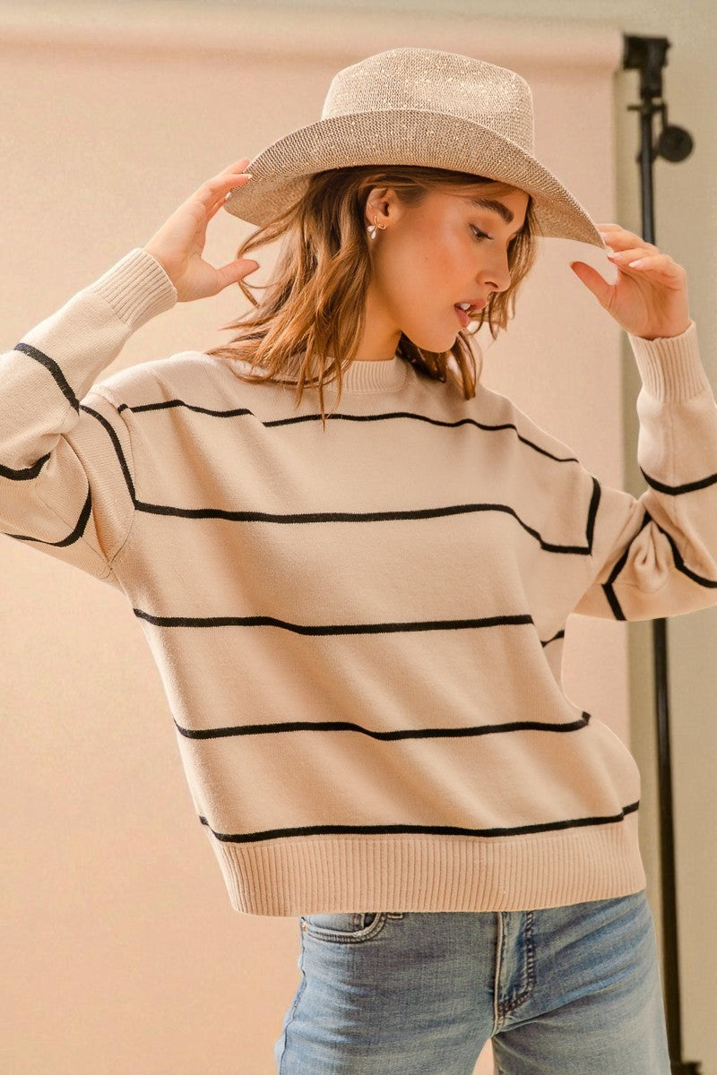 Woman wearing a beige sweater with black stripes and a wide-brimmed hat against a plain background