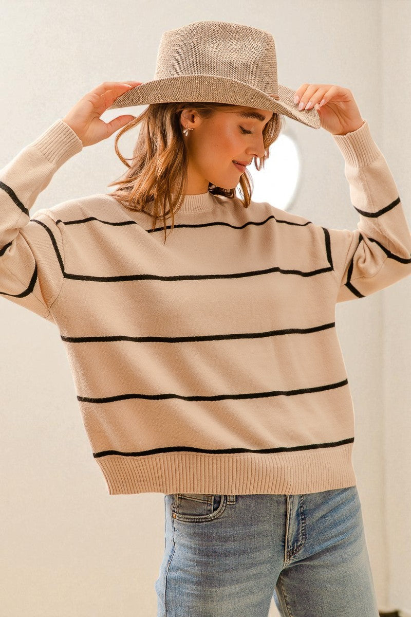 Woman wearing a beige sweater with black stripes and a matching hat against a neutral background