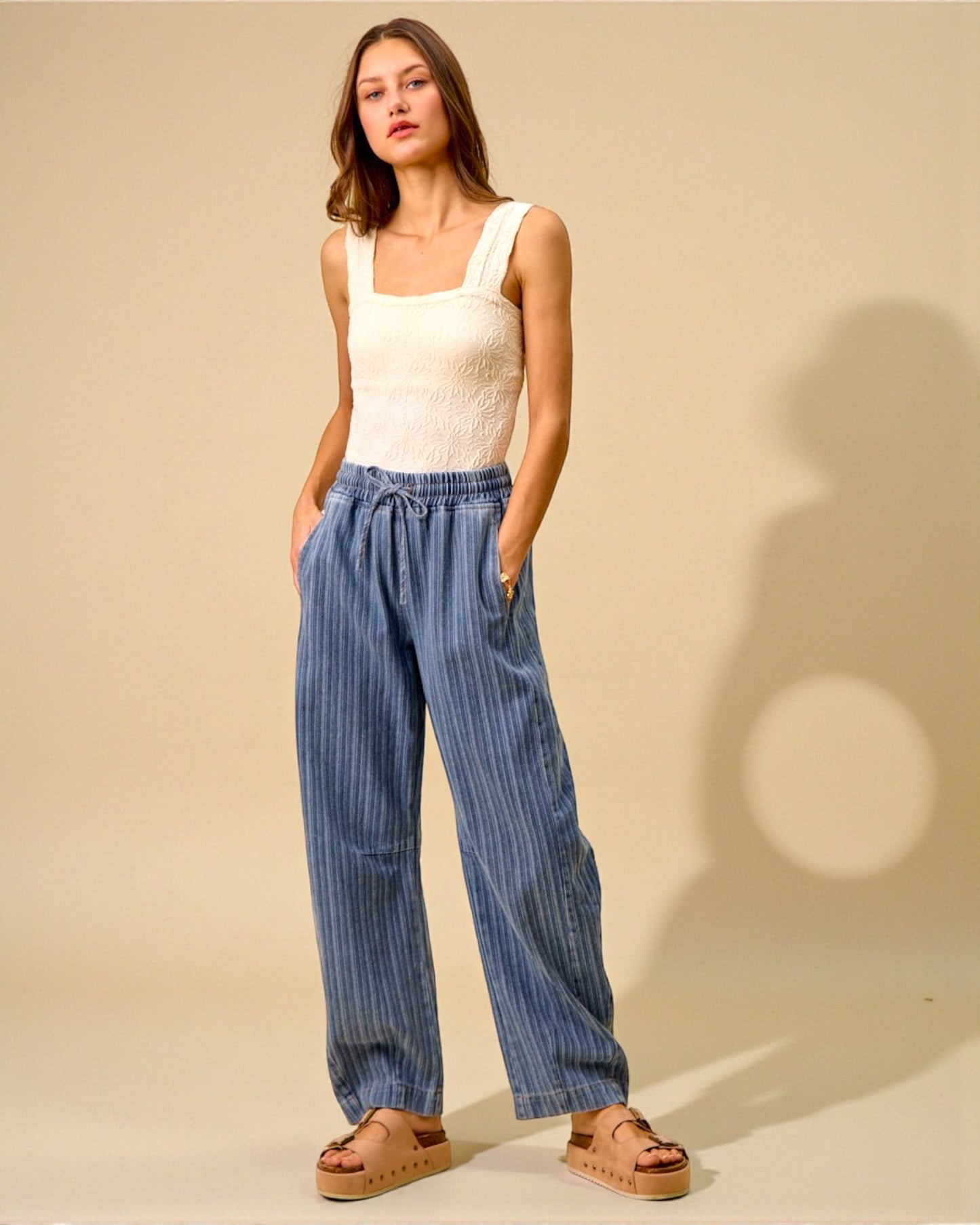 Woman wearing a white sleeveless top and blue wide-leg pants against a beige background