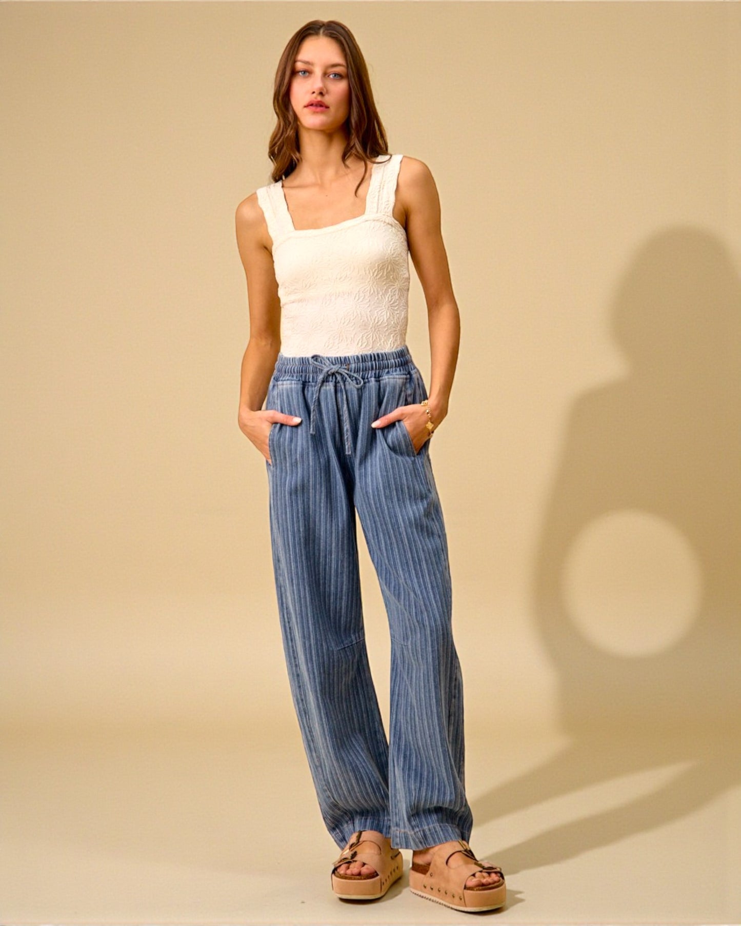 Woman wearing a white tank top and blue striped pants against a beige background