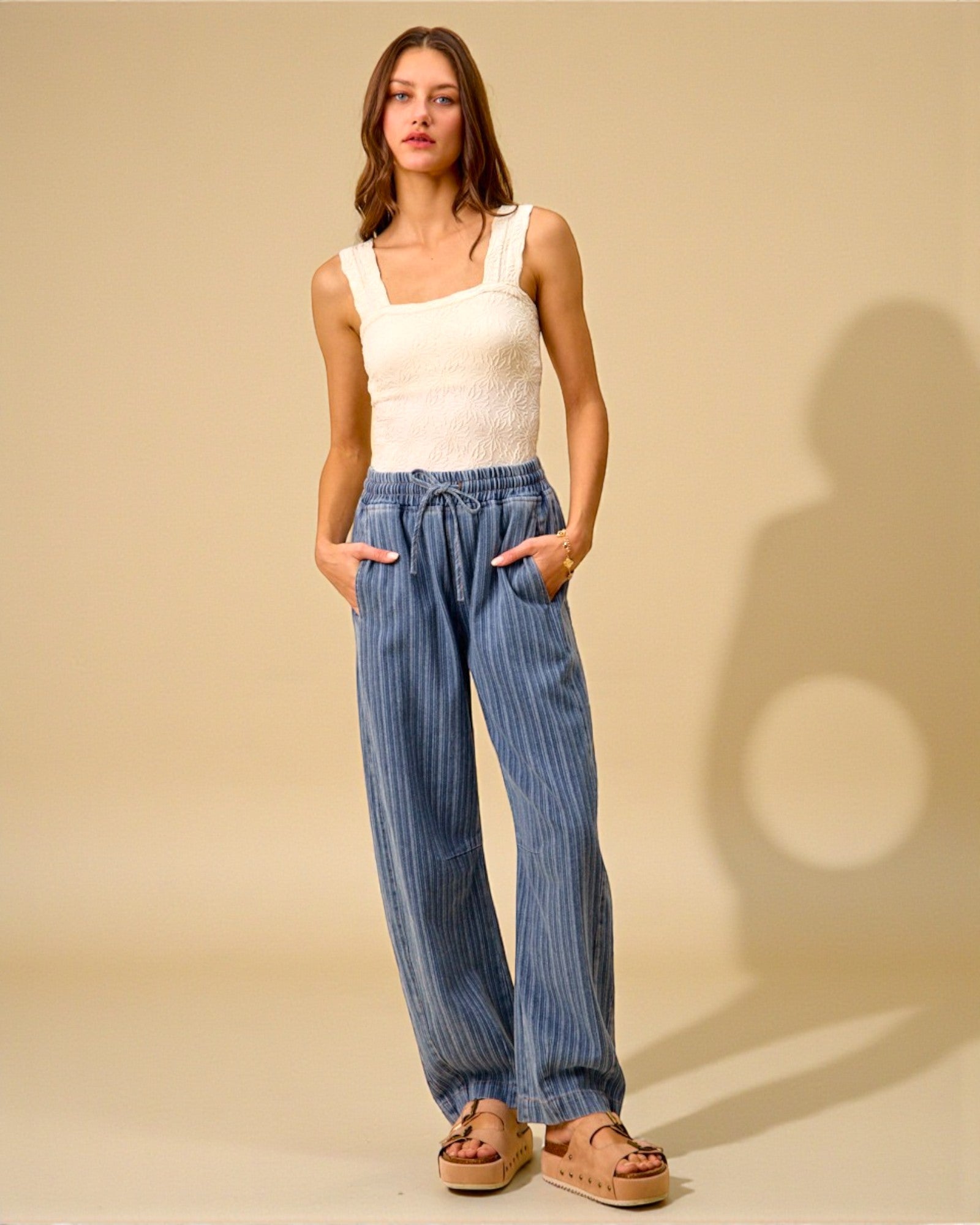 Woman wearing a white tank top and blue striped pants against a beige background