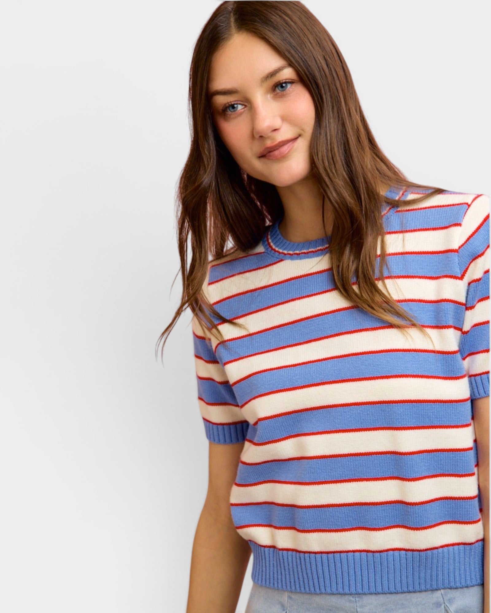 Woman wearing a striped sweater with blue, red, and white colors on a plain background