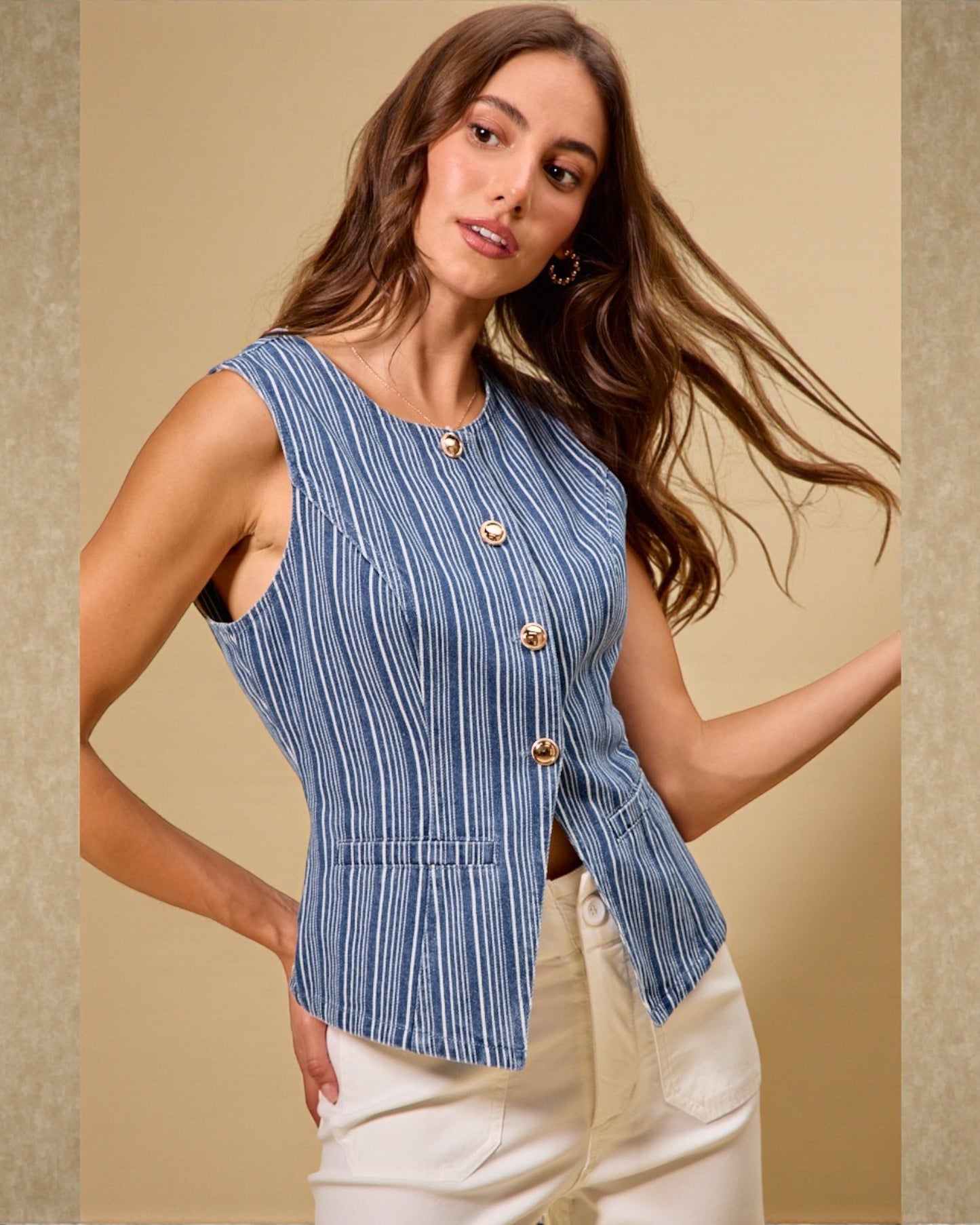 Woman wearing a blue striped sleeveless top with gold buttons against a beige background