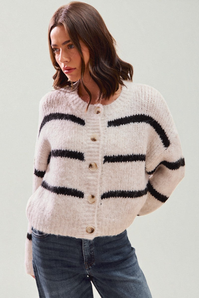 Woman wearing a cream cardigan with black stripes and blue jeans on a light background