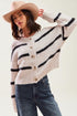 Woman wearing a cream cardigan with black stripes, blue jeans, and a beige hat on a white background