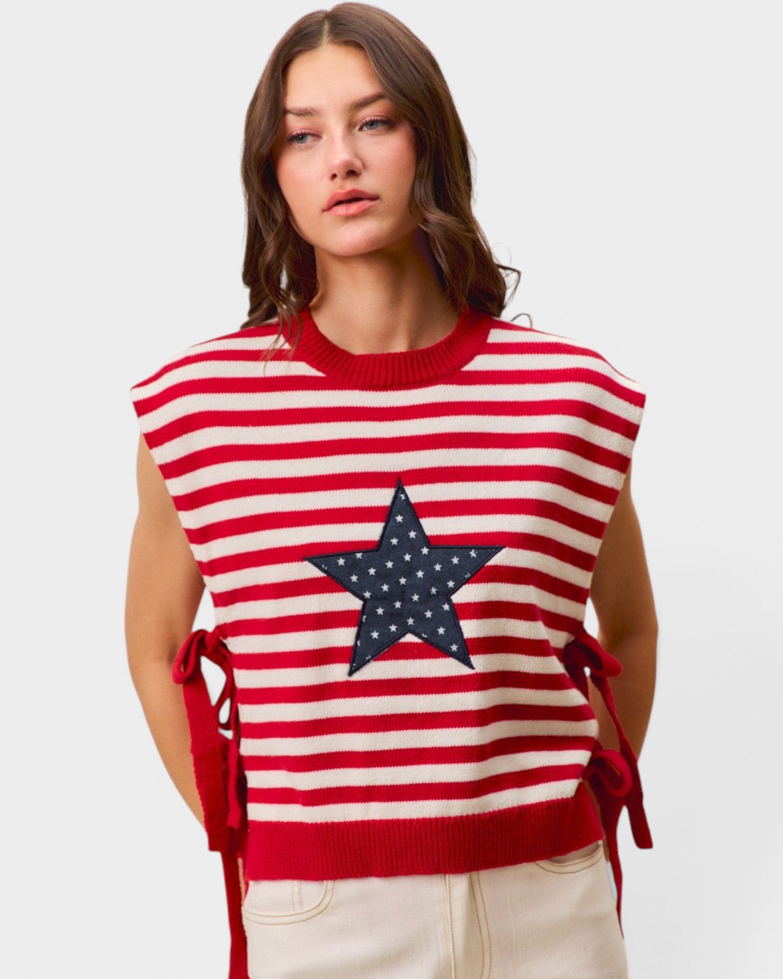 Woman wearing a red and white striped sleeveless sweater with a star design on a plain background