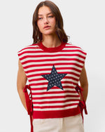 Woman wearing a red and white striped sleeveless sweater with a star design on a plain background