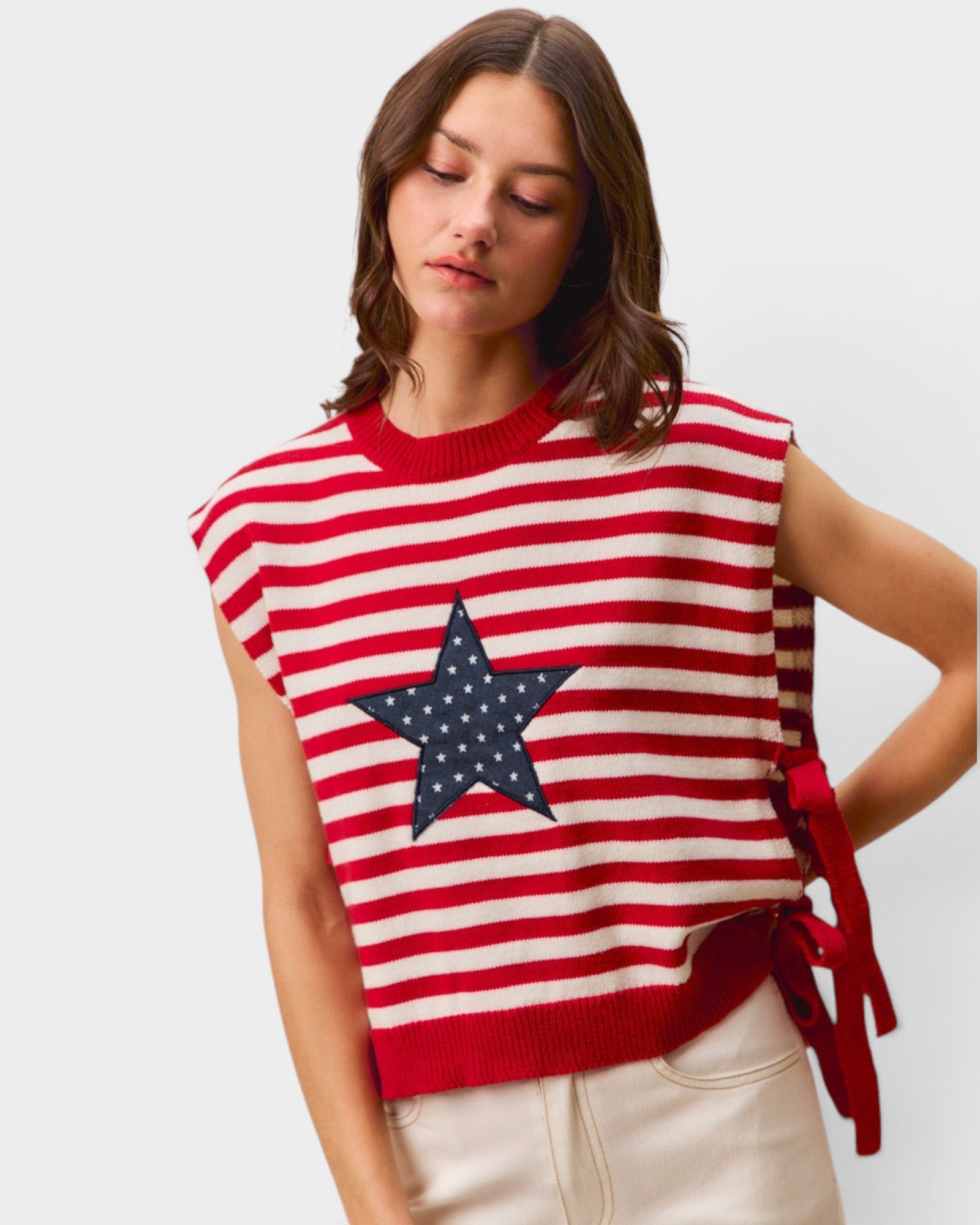 Woman wearing a red and white striped sleeveless sweater with a star design on a plain background