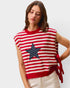 Woman wearing a red and white striped sleeveless sweater with a star design on a plain background