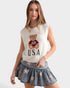 Woman wearing a sleeveless top with a bear graphic and 'USA' text, paired with a denim skirt.