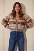 Woman wearing a patterned sweater and blue jeans against a beige wall