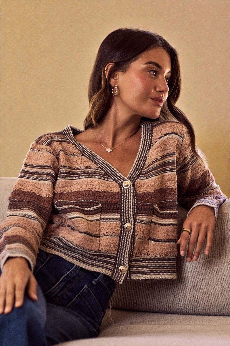 Woman wearing a patterned cardigan sitting on a couch against a beige wall.