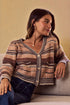 Woman wearing a patterned cardigan sitting on a couch against a beige wall.