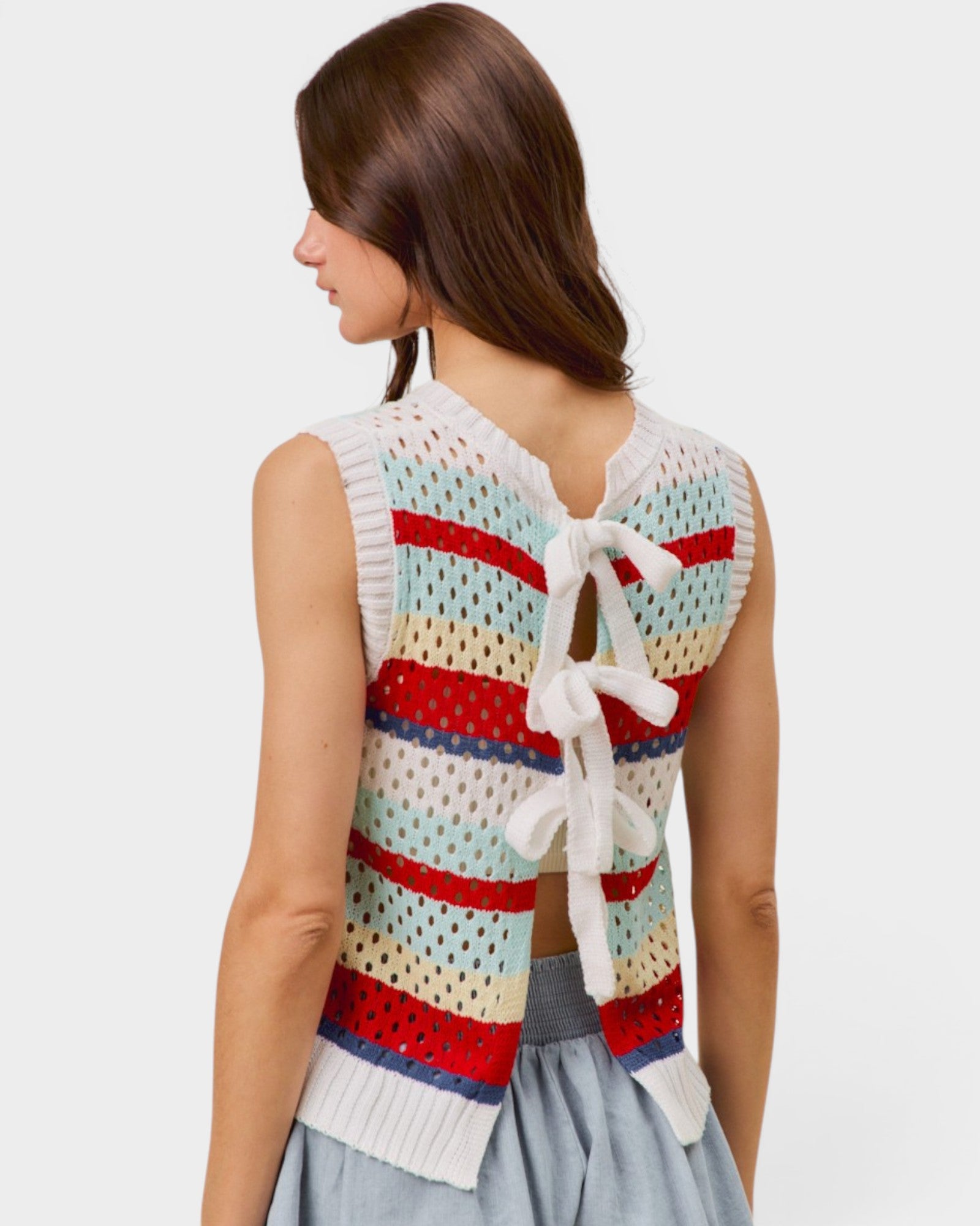Woman wearing a colorful striped sleeveless top with a white lace detail on a light gray background