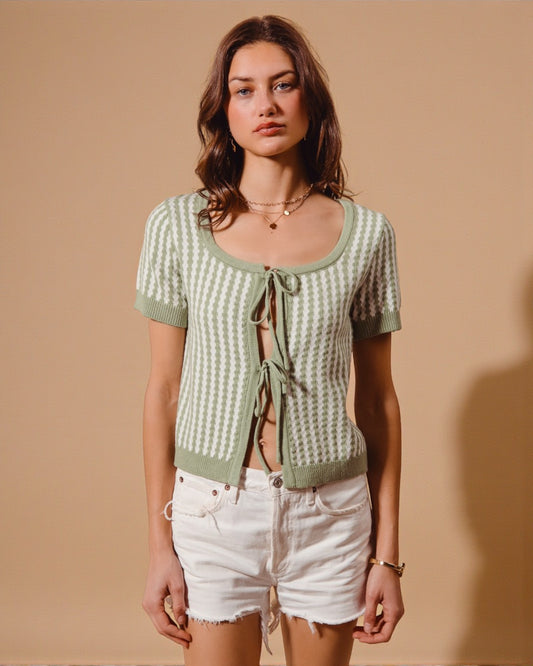 Woman wearing a green patterned cardigan over a black top with white shorts against a beige background