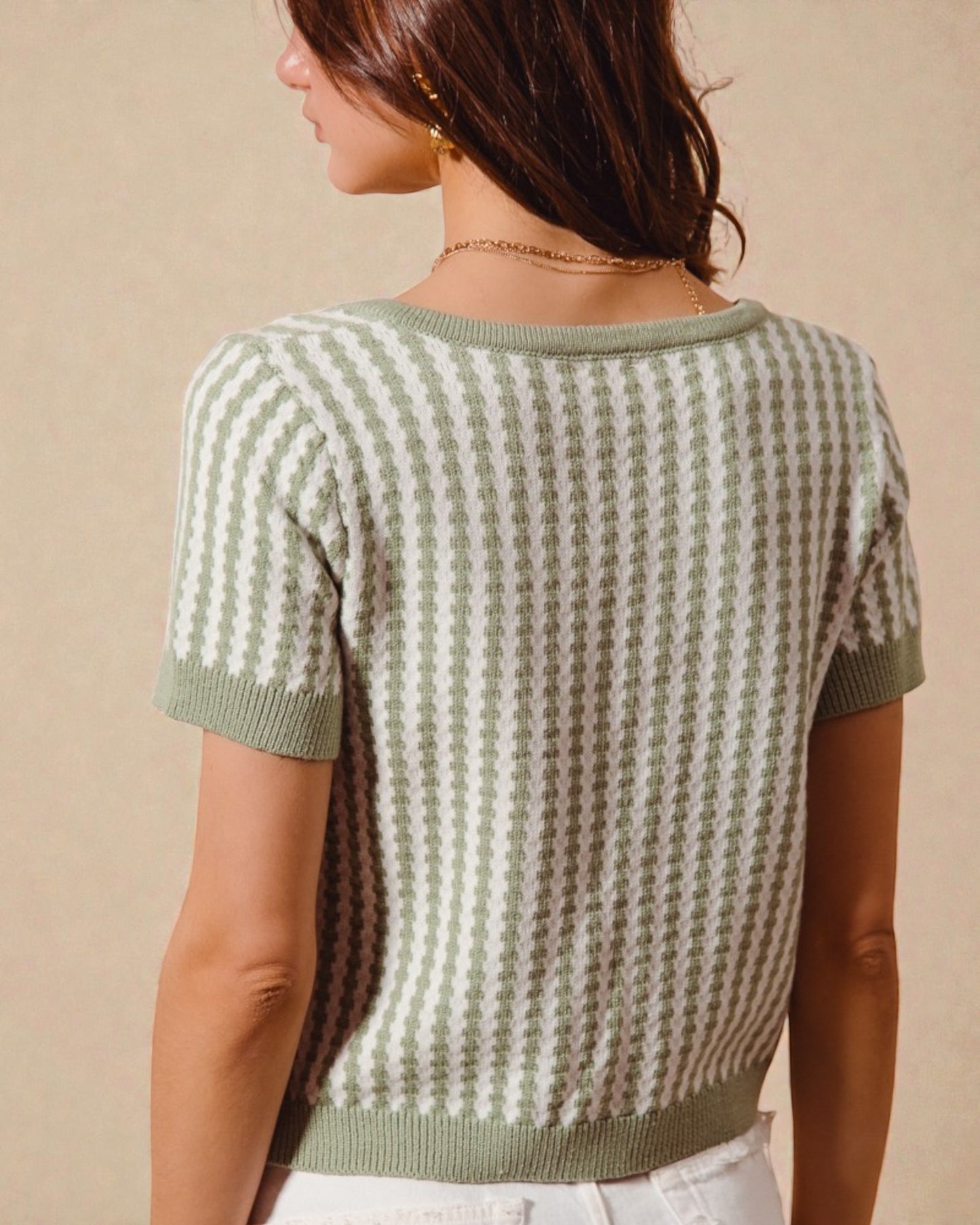 Woman wearing a green and white patterned short-sleeve sweater against a beige background