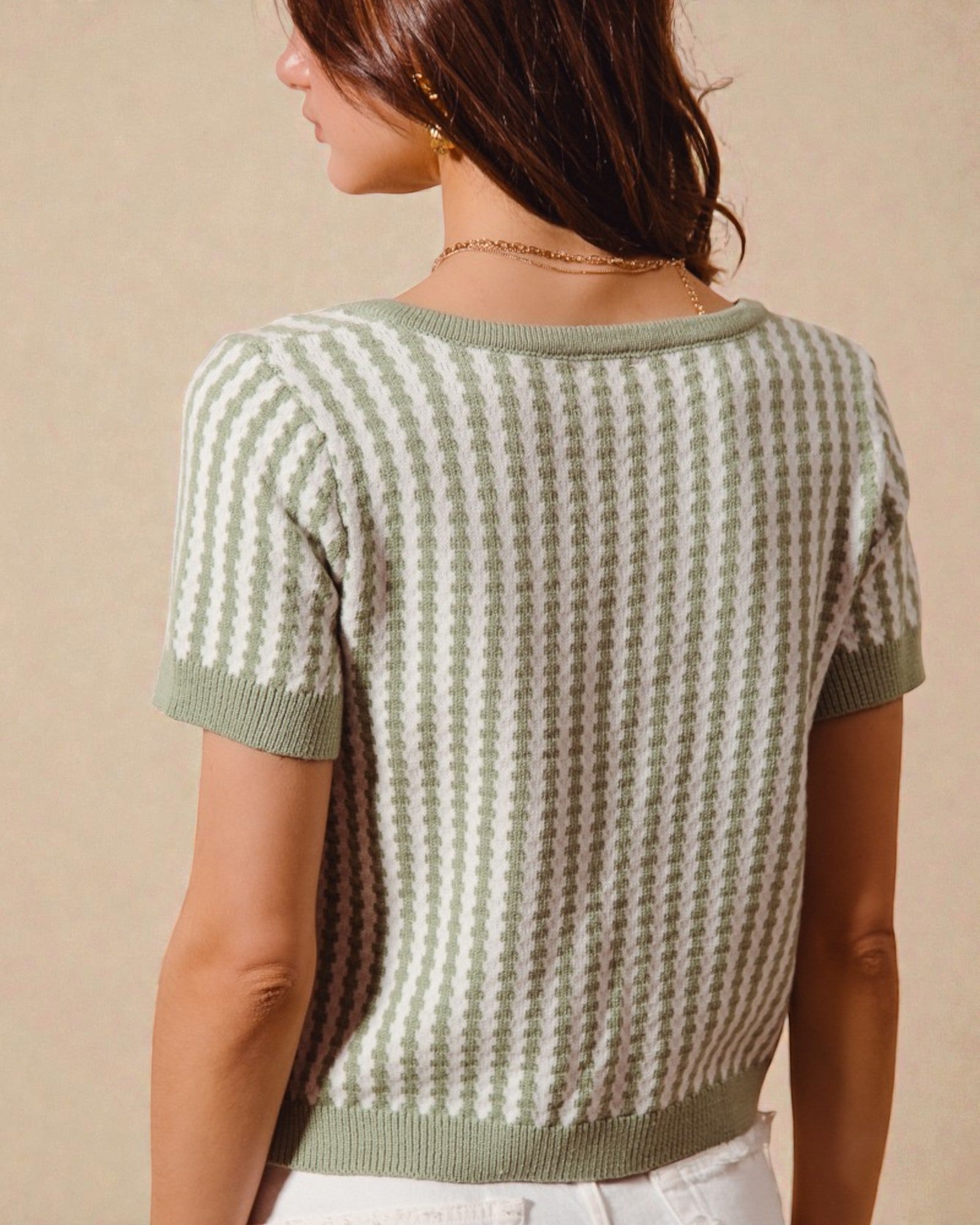 Woman wearing a green and white patterned short-sleeve sweater against a beige background