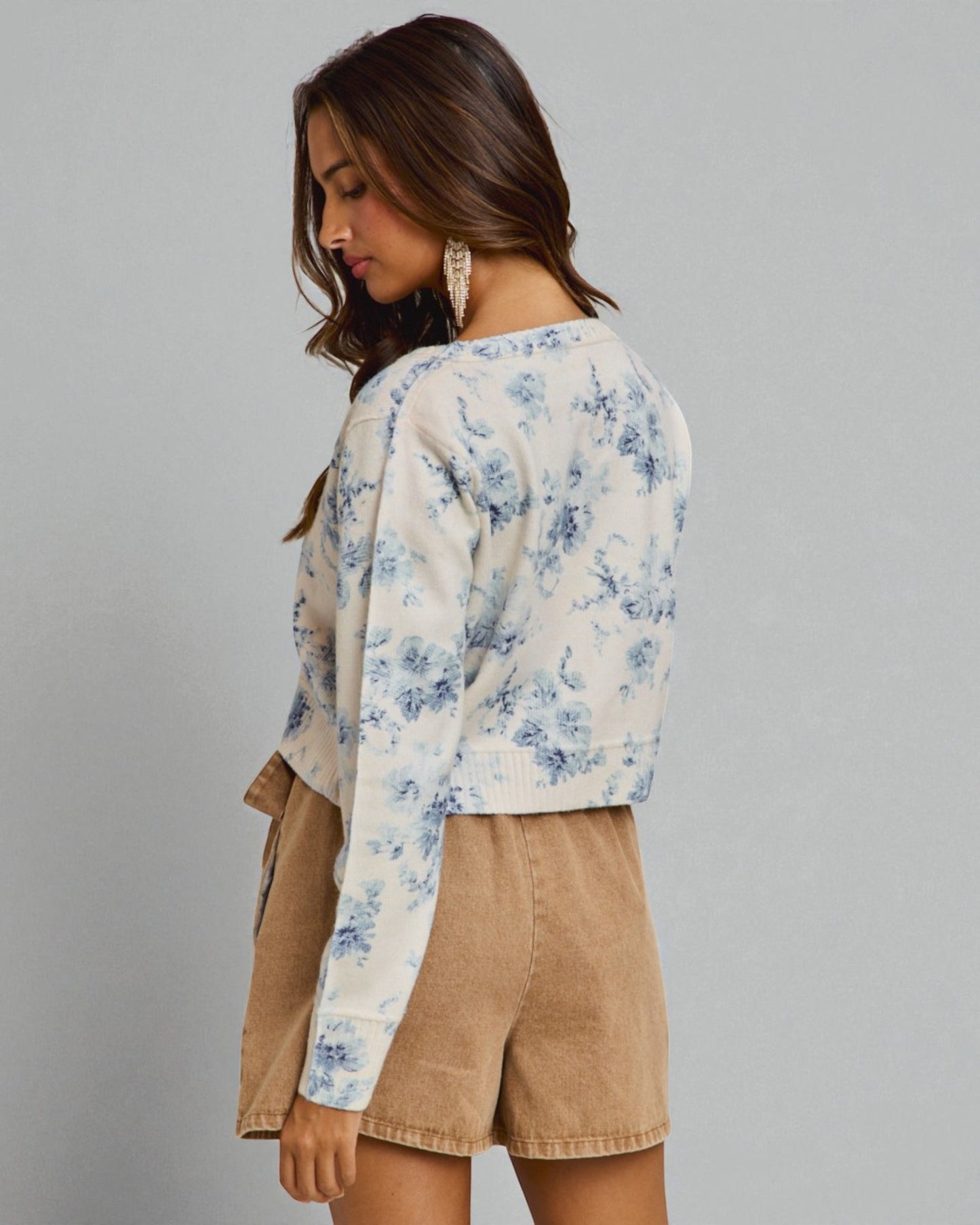 Woman wearing a floral blouse and beige shorts against a gray background