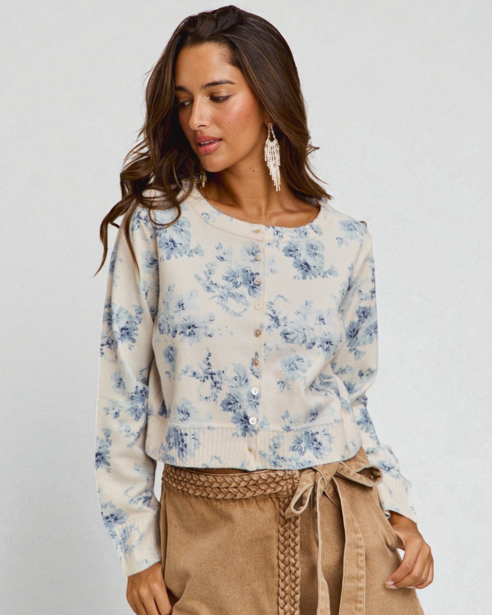 Woman wearing a floral blouse and beige pants against a plain background