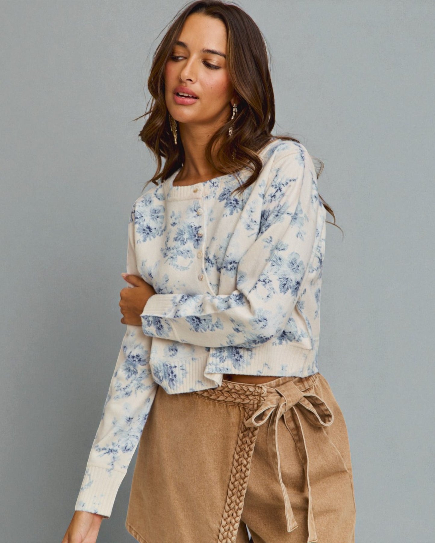 Woman wearing a floral blouse and beige pants against a gray background