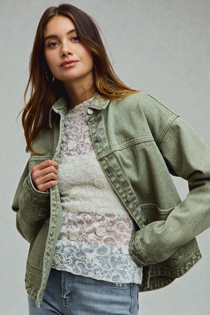 Woman wearing a green denim jacket over a floral top on a gray background