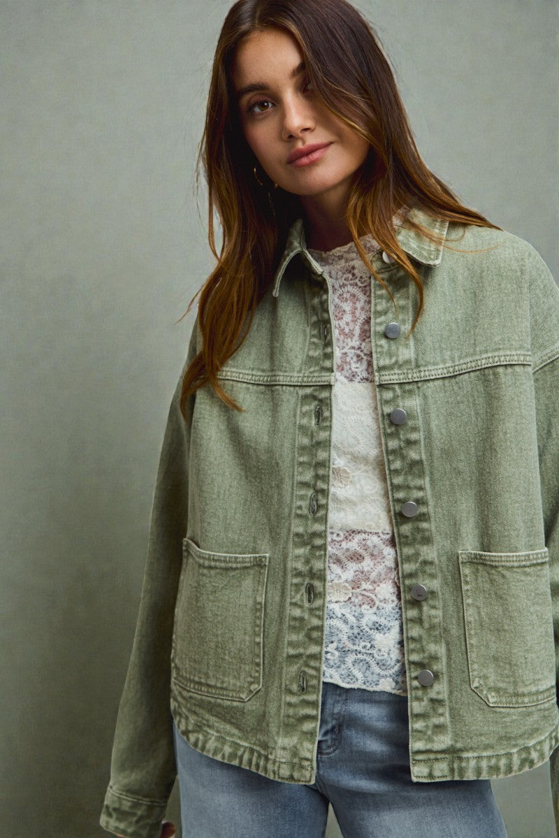 Woman wearing a green denim jacket over a floral shirt against a gray background