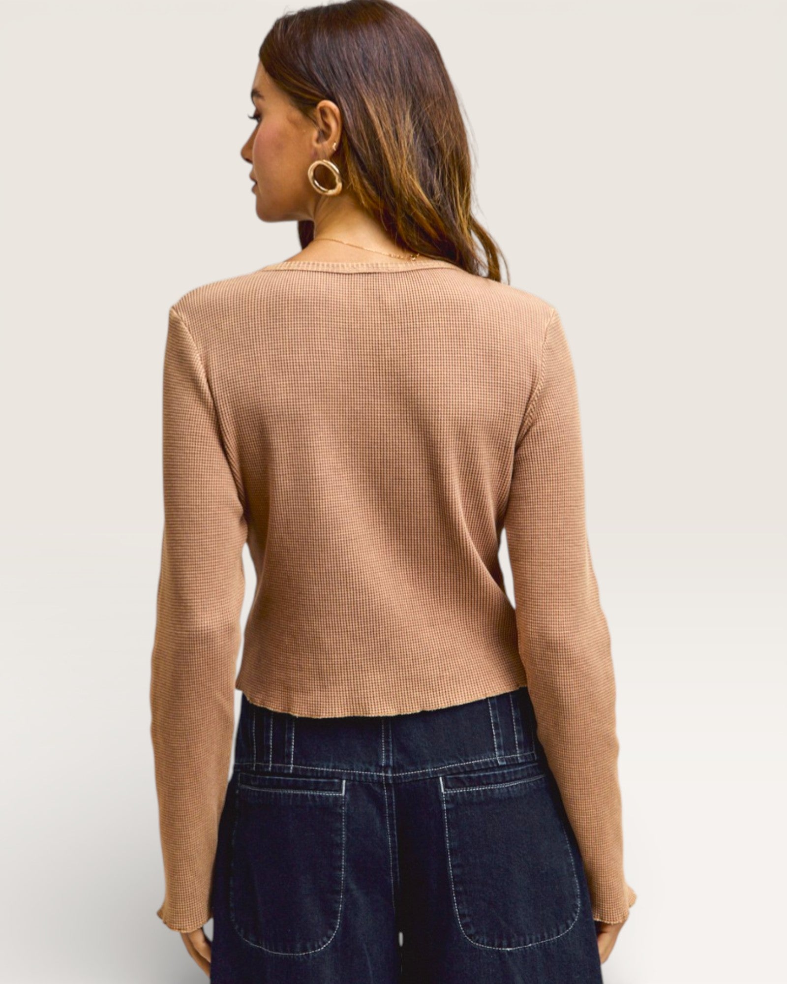 Woman wearing a beige long-sleeve top and dark blue jeans on a light background