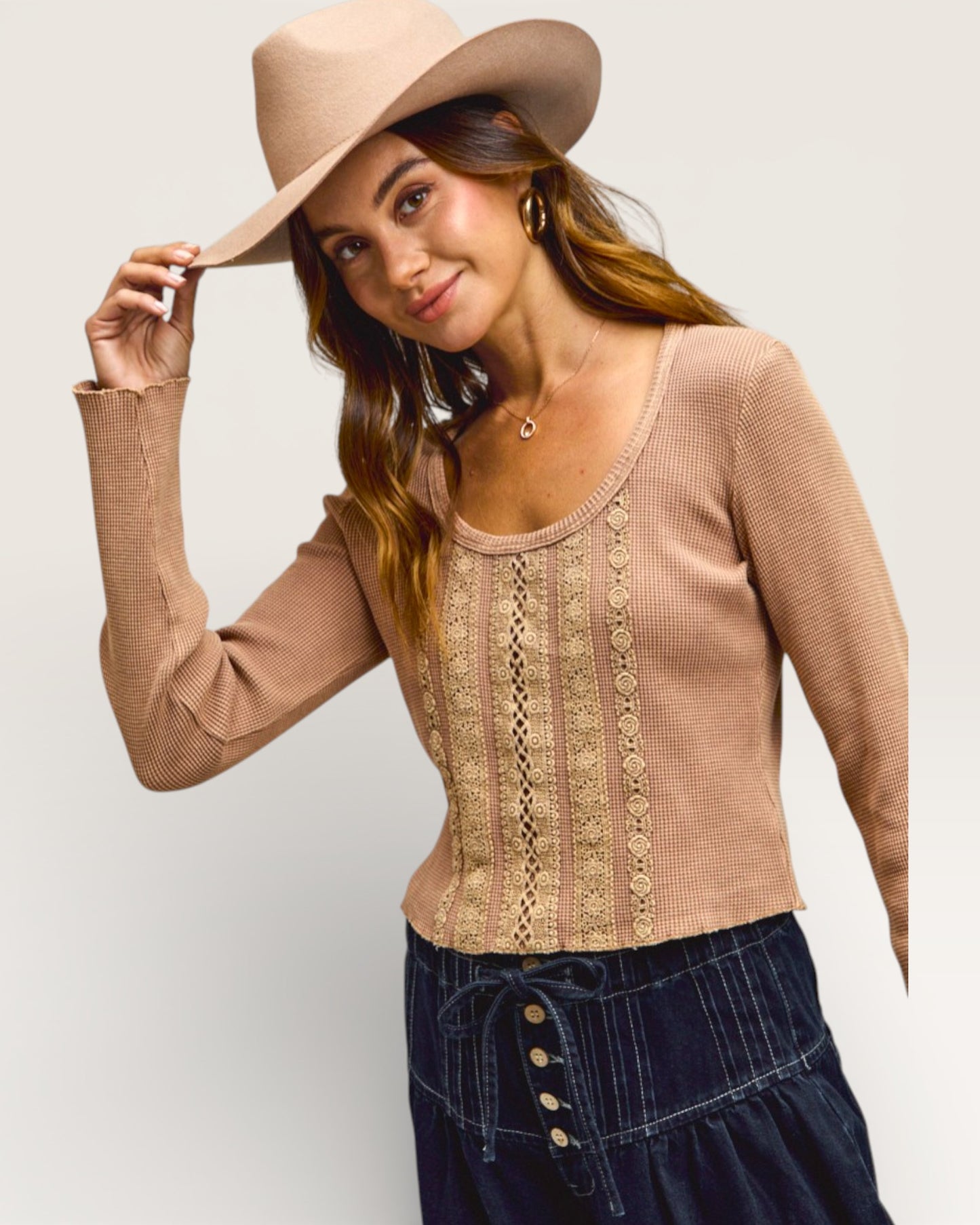 Woman wearing a beige sweater with lace details and a wide-brimmed hat on a plain background