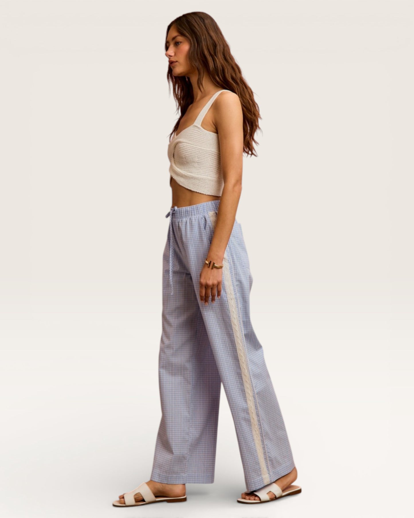 Woman wearing a beige top and light blue checkered pants on a white background