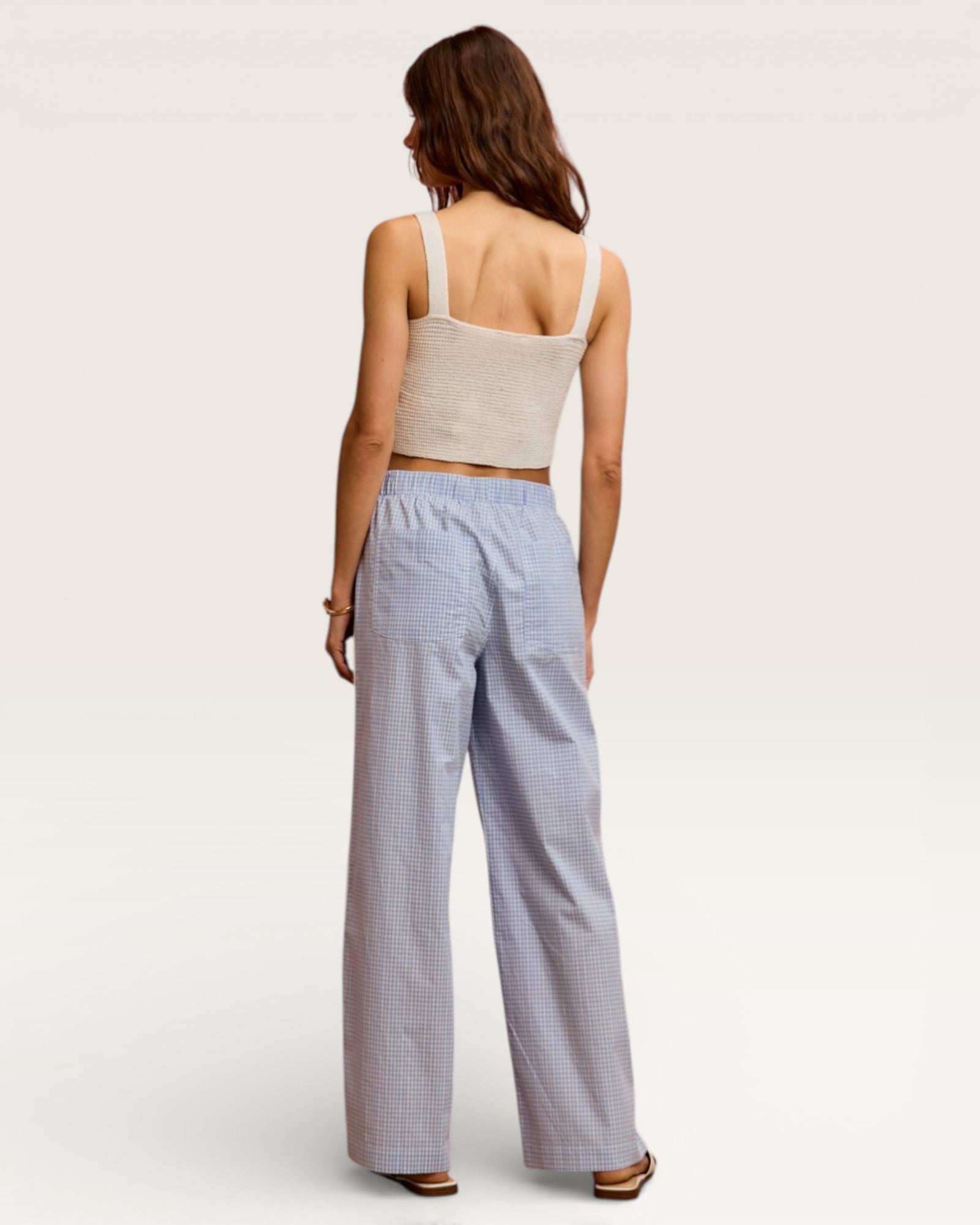 Woman wearing a beige tank top and blue checkered pants on a white background