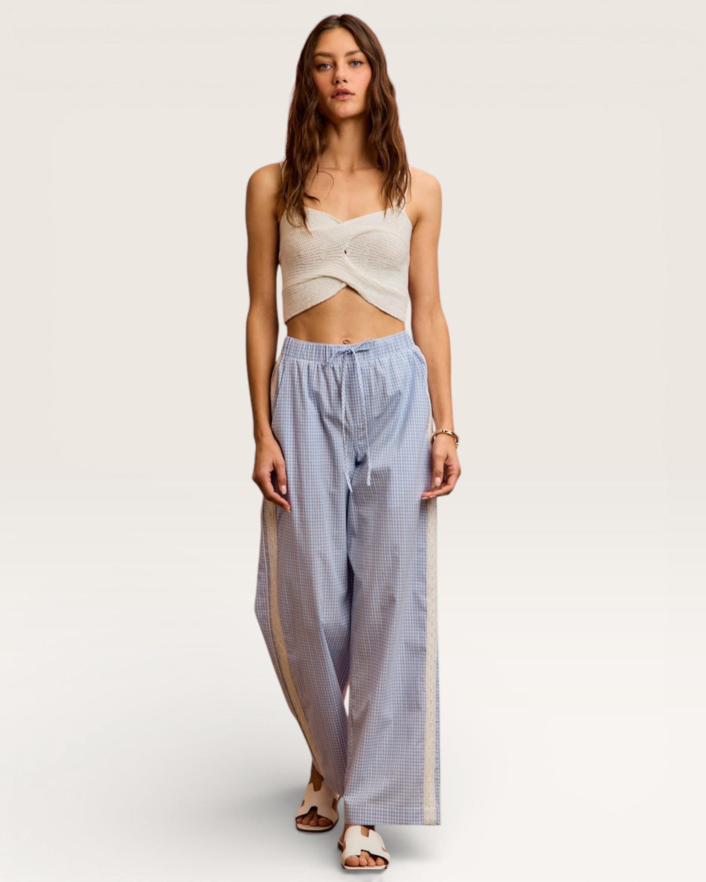 Woman wearing a beige top and light blue checkered pants on a white background