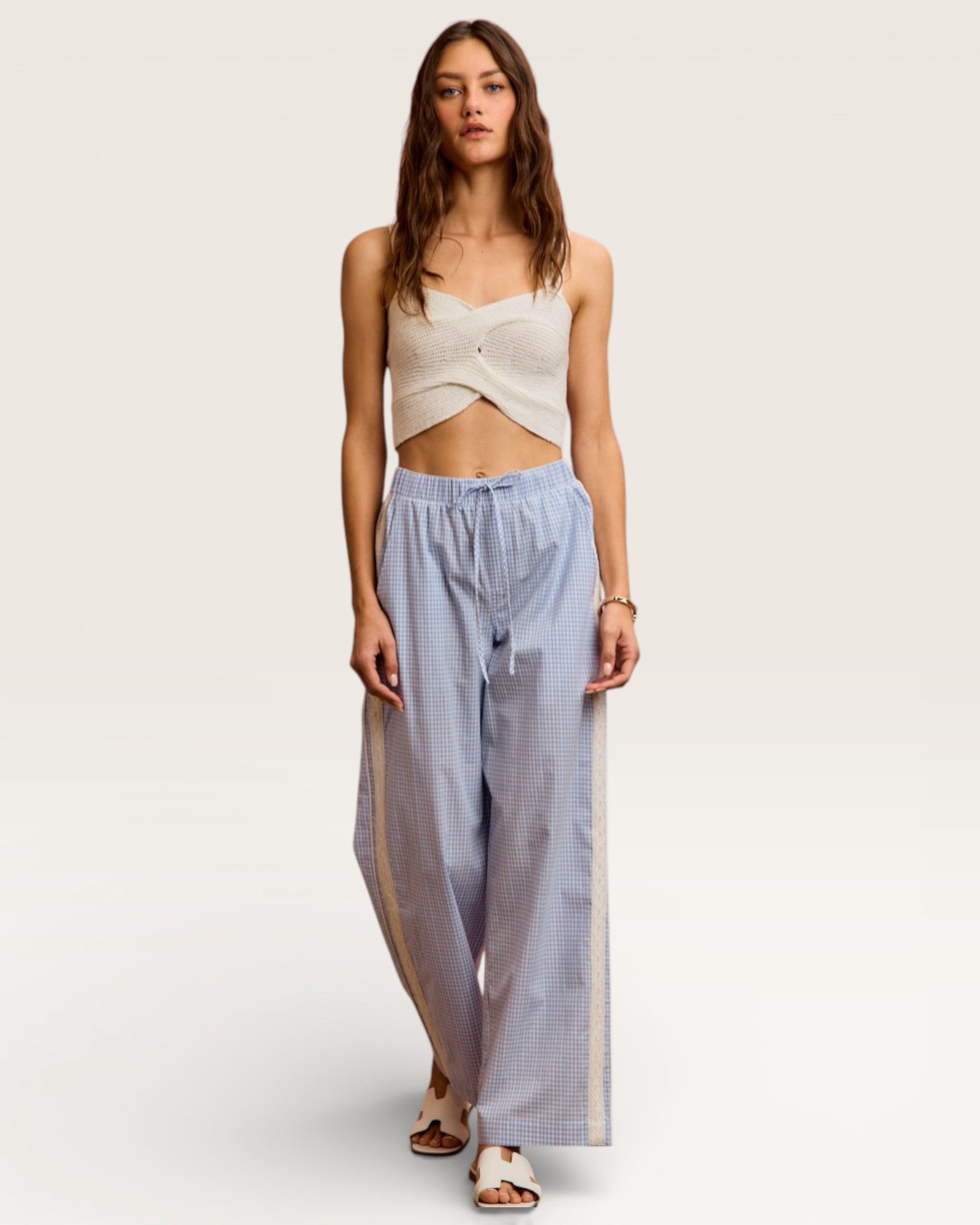 Woman wearing a beige top and light blue checkered pants on a white background