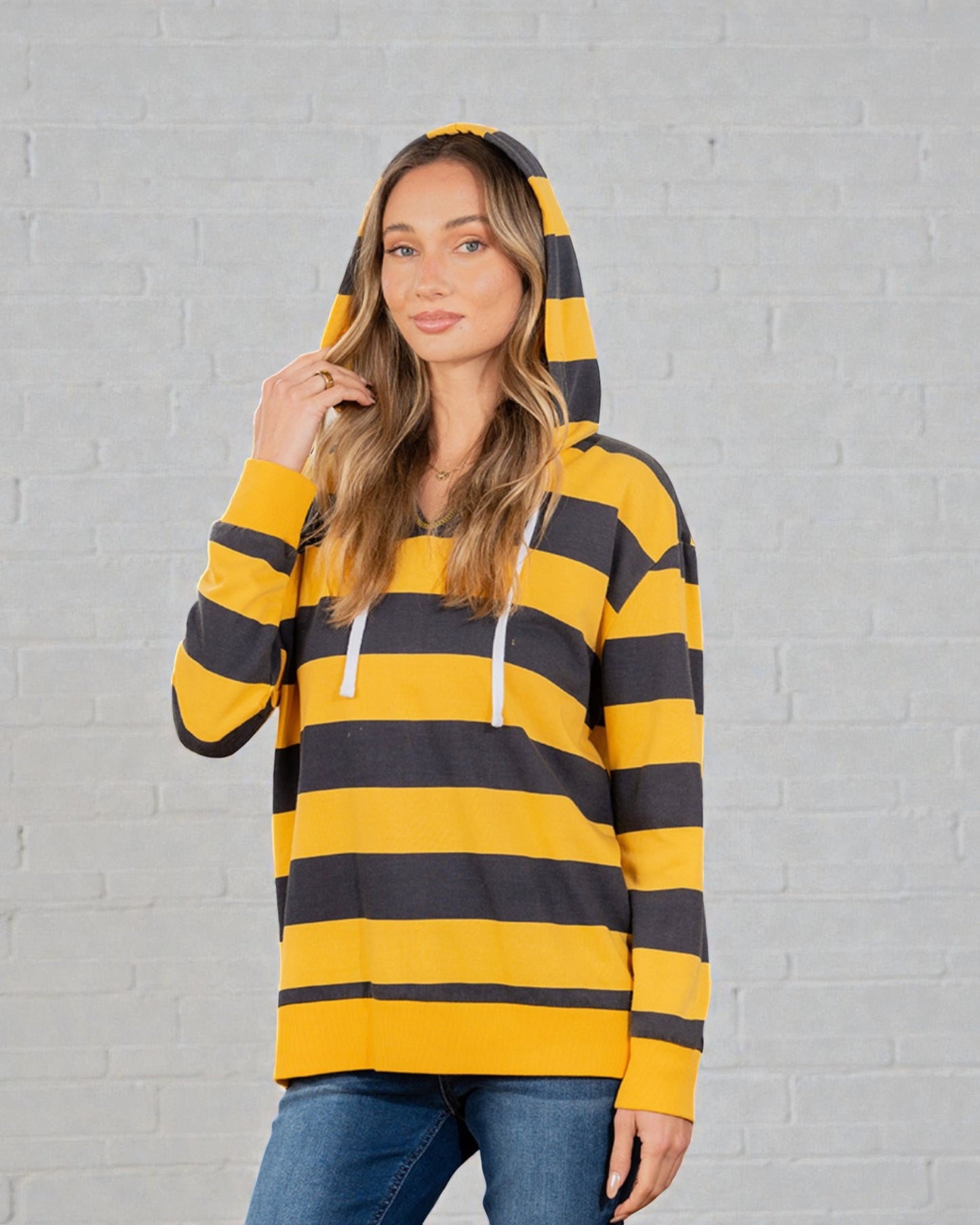 Woman wearing a yellow and black striped hoodie against a gray brick wall.