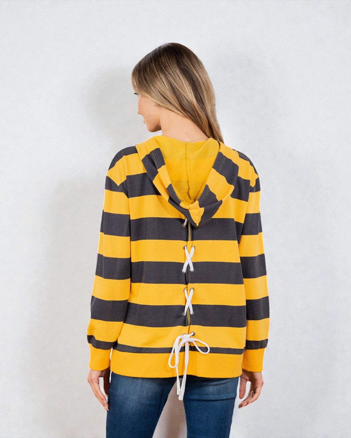 Person wearing a yellow and black striped hoodie with lace-up details on a white background