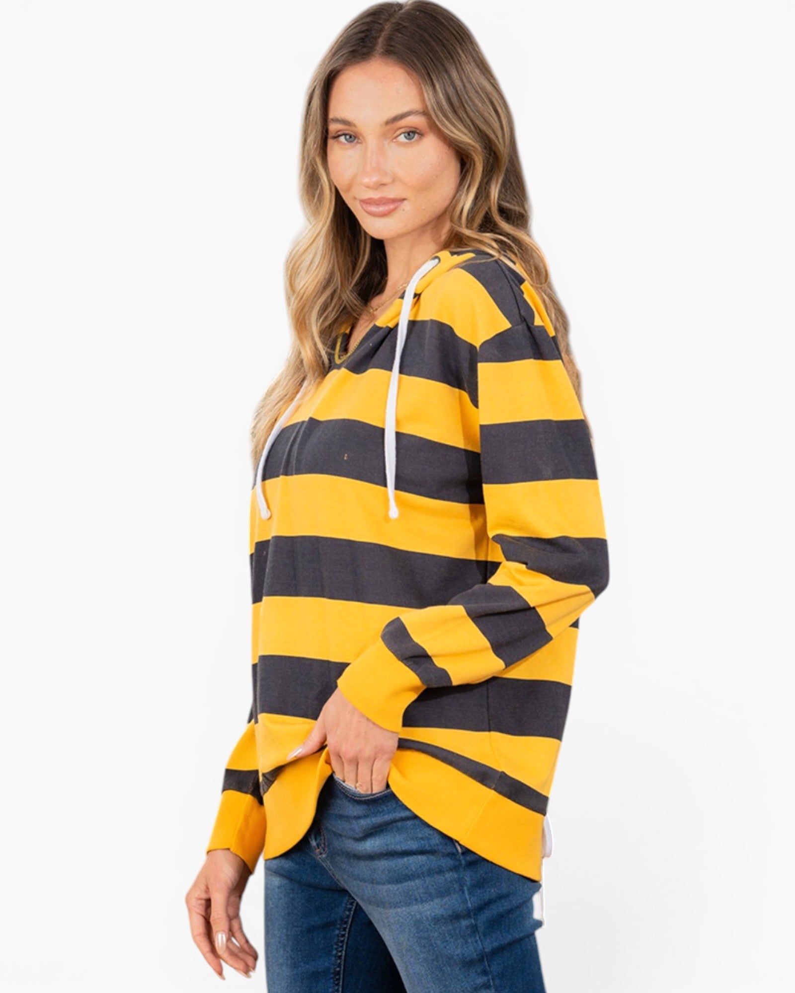 A woman modeling a yellow and black horizontally striped long-sleeve hoodie with white drawstrings, paired with blue jeans, against a plain white studio background.