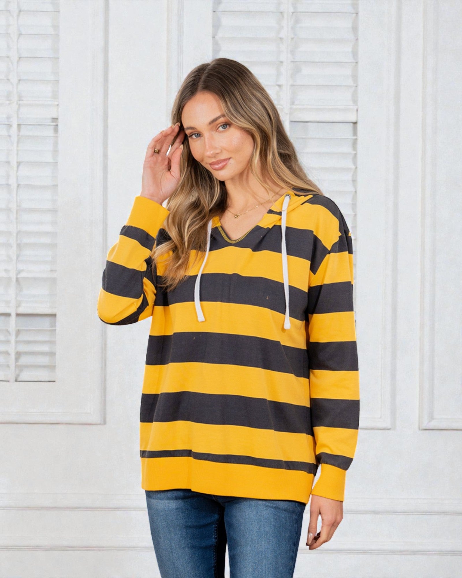 Woman wearing a yellow and black striped hoodie against a white paneled wall.
